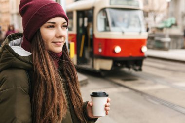 Tramvay durağı yakınında Prag'da sokakta tek kullanımlık bir fincan kahve bir kız içecekler.