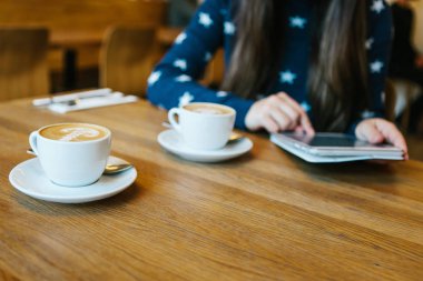 Bir kız bir kafede kahve içer ve bir tablet kullanır