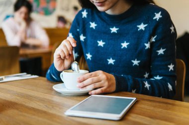 Bir kız bir kafede kahve içer ve bir tablet kullanır