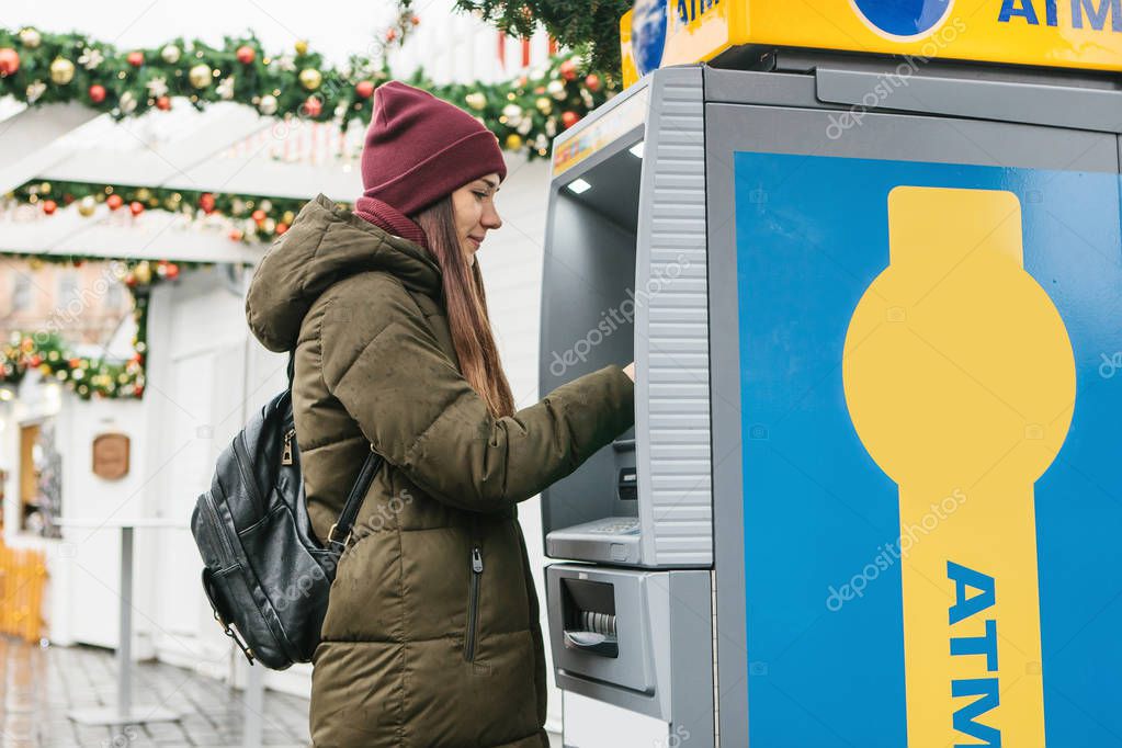 A young woman takes money from an ATM.