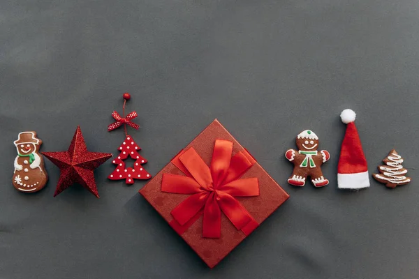 Świąteczna red pudełko z kokardą i obok niego rozmaite ozdoby świąteczne, zabawki i jedzenie. — Zdjęcie stockowe