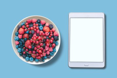 Yukarıdan görüntüleyin. Bir tabak içinde farklı meyveler. Tablet ile çeşitli bir beyaz perde.