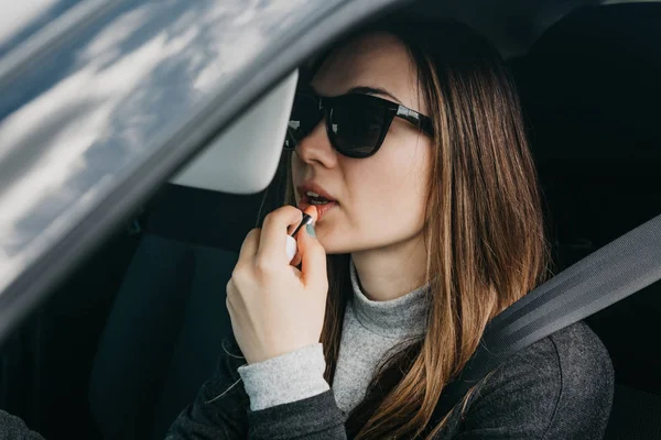 Linda chica joven conductor pinta los labios dentro del coche — Foto de Stock