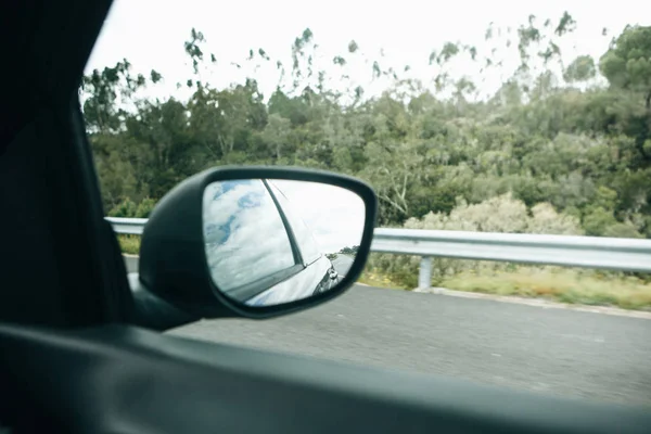Um close-up de um espelho retrovisor do carro enquanto dirige em uma estrada de asfalto ou uma auto-estrada — Fotografia de Stock