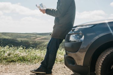 Bir turist adamın arabanın yanında daha fazla seyahat için bölgenin haritasına bakar