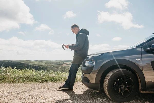 Bir turist adamın arabanın yanında daha fazla seyahat için bölgenin haritasına bakar