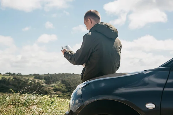 Un turista al lado del coche mira el mapa de la zona para más viajes —  Fotos de Stock