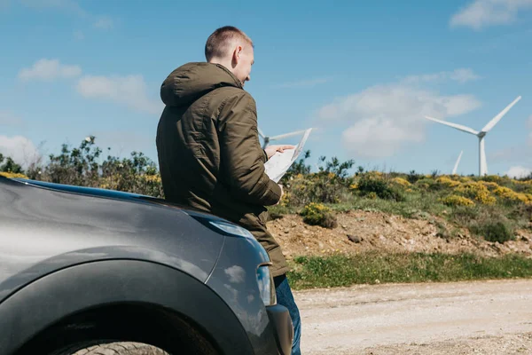 Bir turist adamın arabanın yanında daha fazla seyahat için bölgenin haritasına bakar