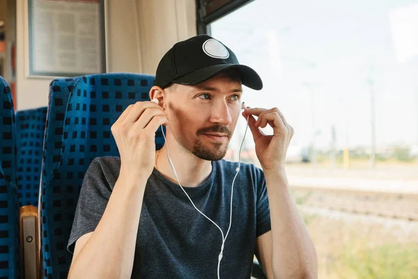 Молодой человек слушает музыку или подкаст во время путешествия в поезде — стоковое фото