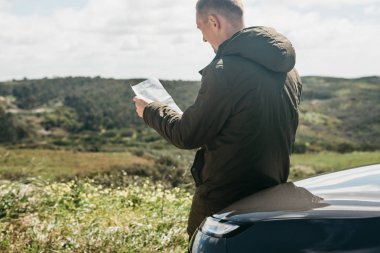 Bir turist adamın arabanın yanında daha fazla seyahat için bölgenin haritasına bakar