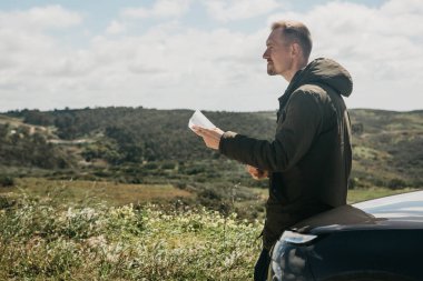 Bir turist adamın arabanın yanında daha fazla seyahat için bölgenin haritasına bakar