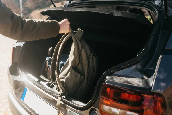 Un uomo o un turista mette uno zaino nel bagagliaio di una macchina. Preparazione per il viaggio. Il concetto di turismo o di viaggio in auto — Foto Stock