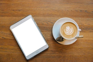 Bir tablet ile boş bir beyaz perde yanındaki masada bir kupa kahve kapuçino
