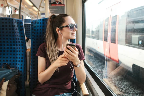 Uma jovem ouve uma música ou podcast enquanto viaja em um trem — Fotografia de Stock
