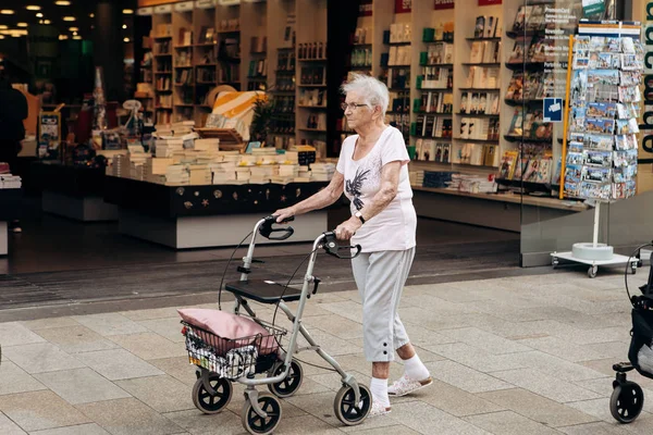 Uma mulher idosa com um carrinho especial para os idosos está andando pela rua . — Fotografia de Stock