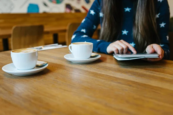 Una chica en un café bebe café y usa una tableta — Foto de Stock