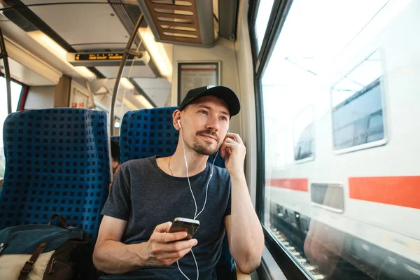 En ung mand lytter til en musik eller podcast, mens han rejser i et tog - Stock-foto