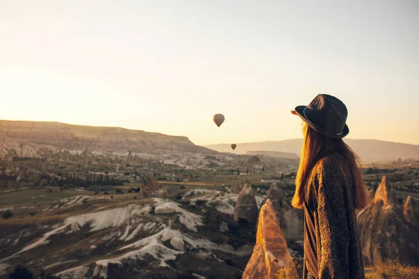 Uma turista de chapéu admira balões de ar quente voando no céu sobre a Capadócia, na Turquia. Visão impressionante. . — Fotografia de Stock