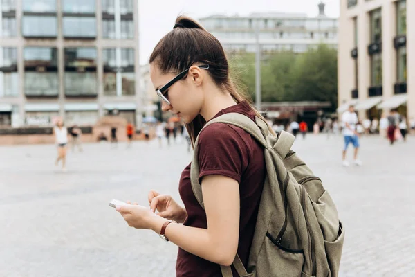 Una chica turística con una mochila utiliza un teléfono móvil — Foto de Stock