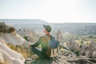 Bir adam bir sırt çantası ile Kapadokya Türkiye'de bir tepe üstünde oturuyor.