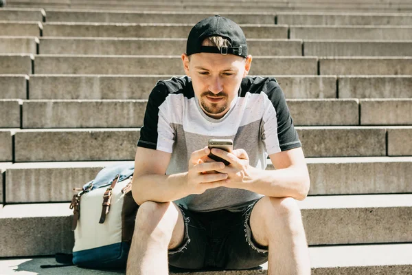 Турист или студент сидит на лестнице, отдыхает и пользуется мобильным телефоном — стоковое фото
