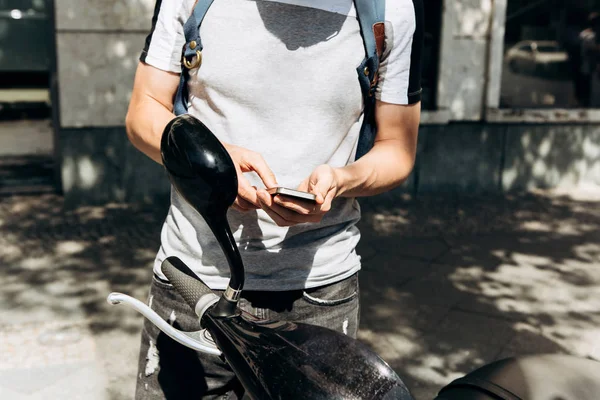 Un chico o un turista activa o alquila un scooter eléctrico usando una aplicación móvil en un teléfono celular . — Foto de Stock