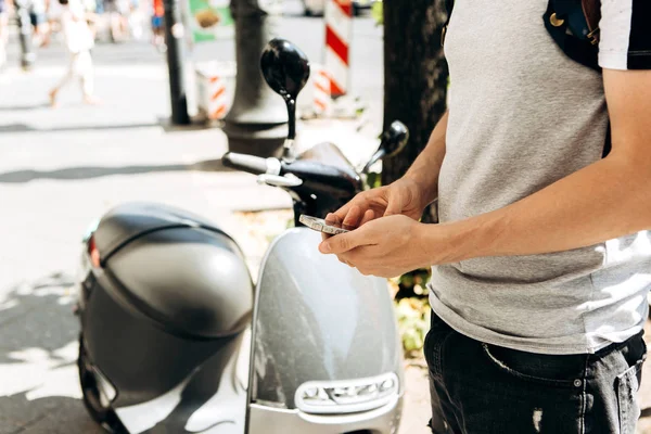 Un gars ou un touriste active ou loue un scooter électrique à l'aide d'une application mobile sur un téléphone portable . — Photo