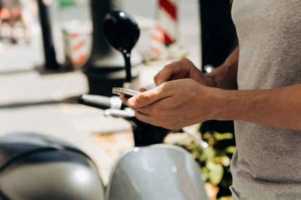 Een kerel of een toeristische activeert of verhuurt een elektrische scooter met behulp van een mobiele applicatie op een mobiele telefoon. — Stockfoto