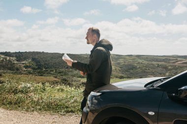 Bir turist adamın arabanın yanında daha fazla seyahat için bölgenin haritasına bakar