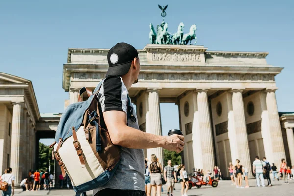 Seseorang memegang cangkir sekali pakai dengan kopi atau minuman lain di latar belakang Gerbang Brandenburg di Berlin . — Stok Foto