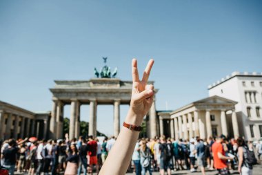 Kız Brandenburg Kapısı ve bulanık tanınmayan insanları Almanya Berlin'de arka plan üzerinde barış işareti gösterir.