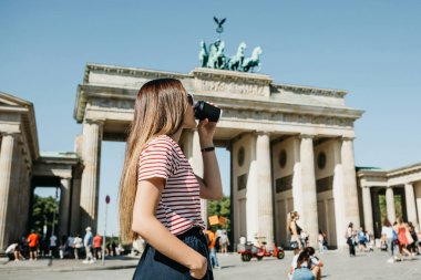 Bir kişi tek kullanımlık bir fincan kahve ya da Berlin Brandenburg Kapısı'nın arka planda başka bir içecek ile tutar.
