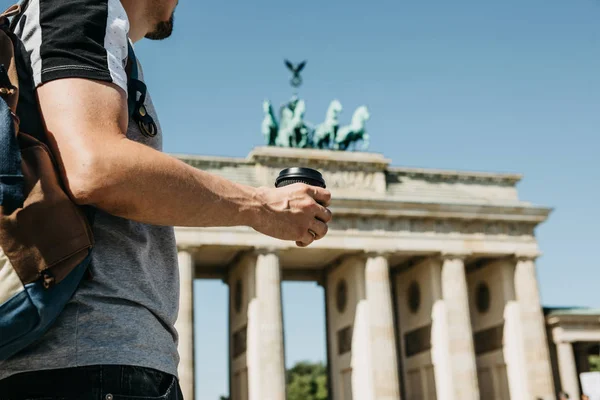 Una persona sostiene una taza desechable con café u otra bebida en el fondo de la Puerta de Brandeburgo en Berlín . — Foto de Stock