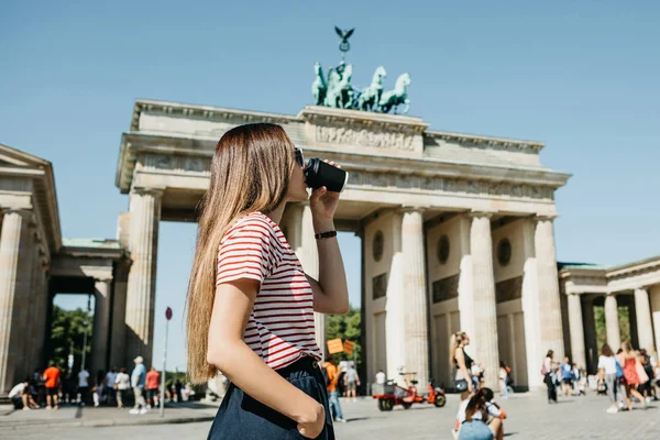 Una persona sostiene una taza desechable con café u otra bebida en el fondo de la Puerta de Brandeburgo en Berlín . — Foto de Stock