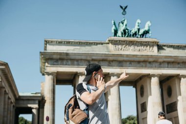 Bir turist ya da bir adam bir sırt çantası ile bir cep telefonu üzerinde konuşurken ve Berlin Brandenburg Kapısı üzerinde elini gösterir