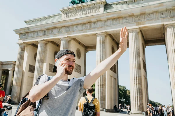 Un turista o un tipo con una mochila está hablando en un teléfono móvil y está saludando a alguien con su mano . — Foto de Stock