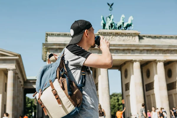 Una persona sostiene una taza desechable con café u otra bebida en el fondo de la Puerta de Brandeburgo en Berlín . — Foto de Stock