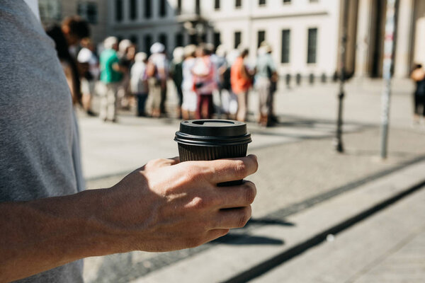 Closeup of a man on a city street holding a coffee or other takeaway drink in his hand.