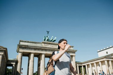 Bir kişi tek kullanımlık bir fincan kahve ya da Berlin Brandenburg Kapısı'nın arka planda başka bir içecek ile tutar.