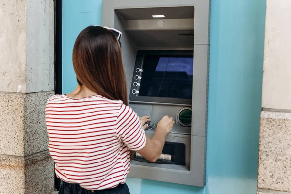 Una mujer joven toma dinero de un cajero automático. Toma una tarjeta del cajero automático. Finanzas, tarjeta de crédito, retiro de dinero . — Foto de Stock