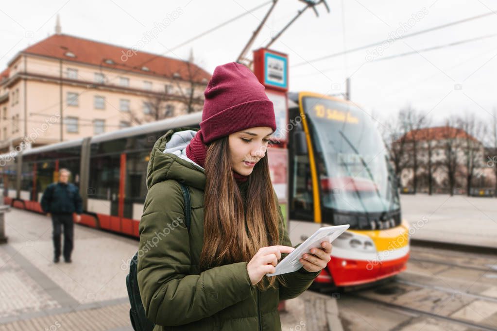 Beautiful tourist girl with a tablet on a street in Prague looks at a map or uses the Internet or a mobile application.