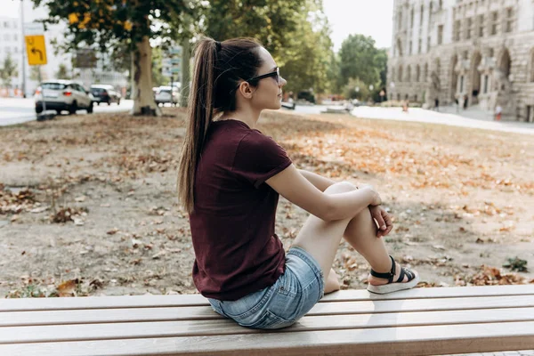 Молода красива дівчина сидить на лавці на вулиці і відпочиває . — стокове фото