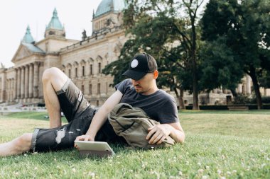 Genç bir adam çim üzerinde yalan ve internette sörf veya çevrimiçi ya da başka bir şey.