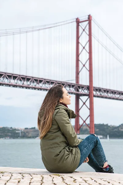 Dívka v saku na nábřeží v Lisabonu v chladném počasí sedí zavřel oči a snít — Stock fotografie