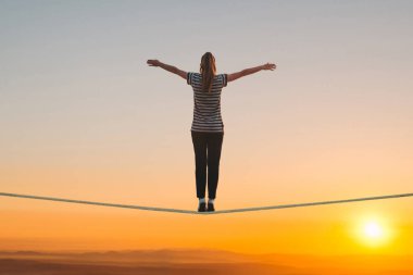 A girl stands on the rope and raises her hands against the sunset. clipart