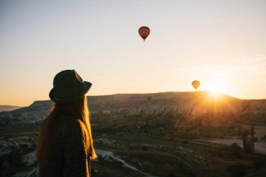 Şapkalı bir turist kız sıcak hava balonları Türkiye Kapadokya'da üzerinde gökyüzünde uçan hayran. Etkileyici görüş.