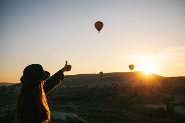Şapkalı bir turist kız sıcak hava balonları Türkiye Kapadokya'da üzerinde gökyüzünde uçan hayran. Etkileyici görüş.