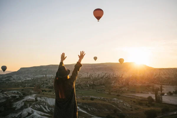 Uma turista de chapéu admira balões de ar quente voando no céu sobre a Capadócia, na Turquia. Visão impressionante. . — Fotografia de Stock