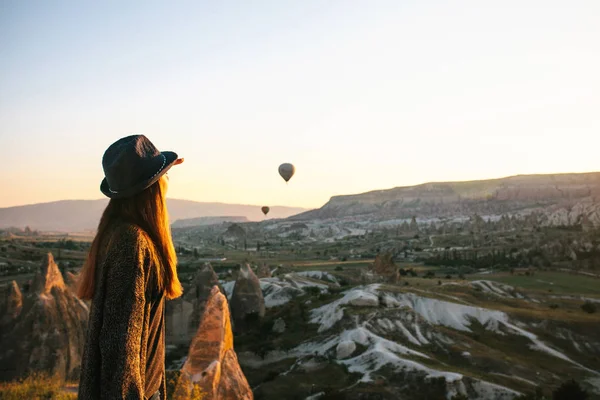 Een toeristische meisje in een hoed bewondert hete lucht ballonnen in de lucht vliegen over Cappadocië in Turkije. Indrukwekkend gezicht. — Stockfoto