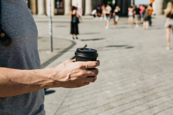 Closeup of a man on a city street holding a coffee or other takeaway drink in his hand.